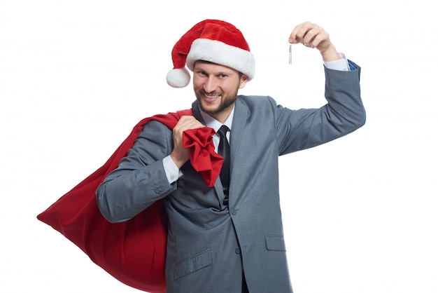 Smiling man in suite and red cap, holding bag with presents over shoulder and showing key.