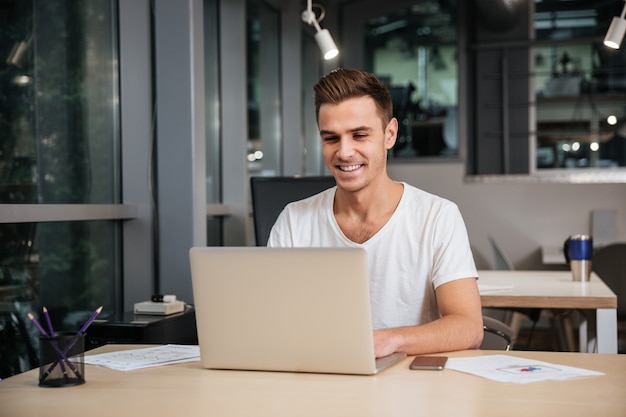 Smiling Man in t-shirt working in office with laptop computer.