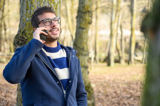 Smiling man, talking on mobile phone in an autumn park.