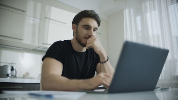 Smiling man using laptop computer at kitchen table Young business man smiling