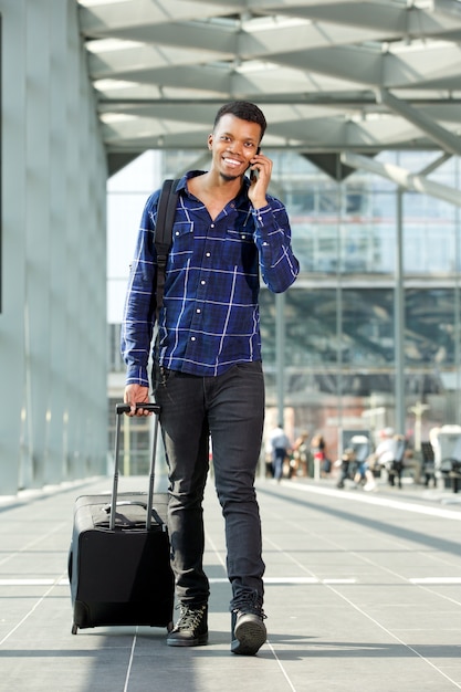 Photo smiling man walking with suitcase talking on mobile phone