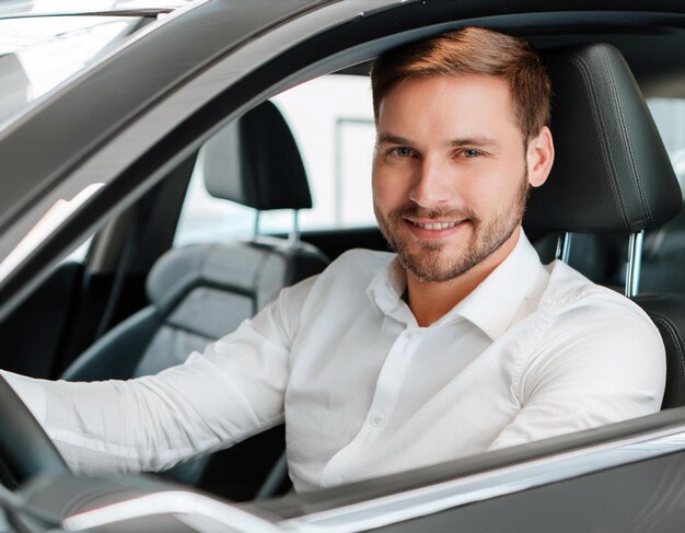 Photo smiling man in white shirt sits in modern car during daytime at dealership