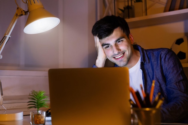 Smiling man wirking with laptop at night at home