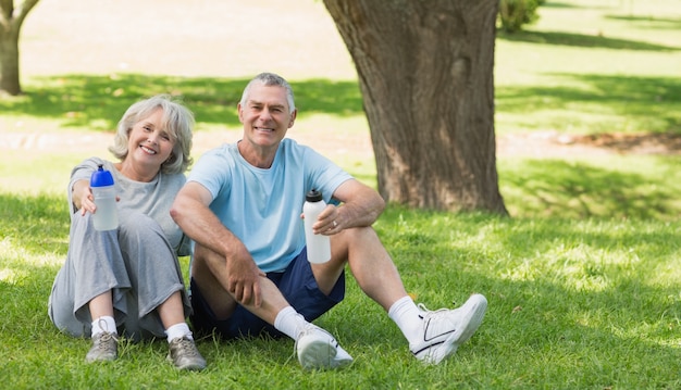 Smiling mature couple sitting with water bottles at park