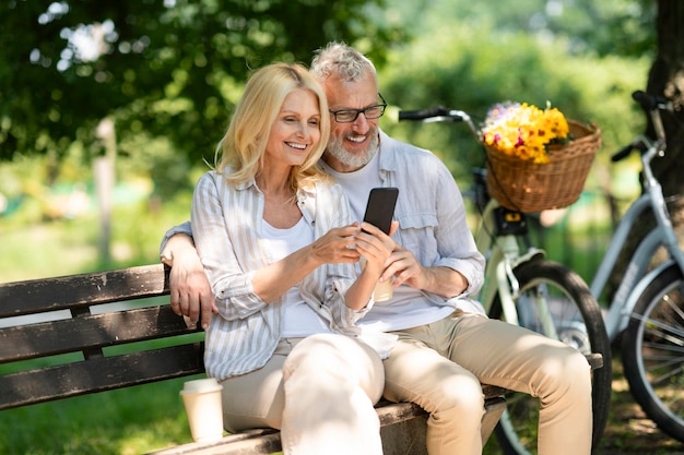 Smiling mature couple using smartphone while relaxing on bench in park