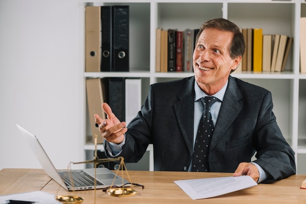 Smiling mature lawyer holding document in hand at workplace