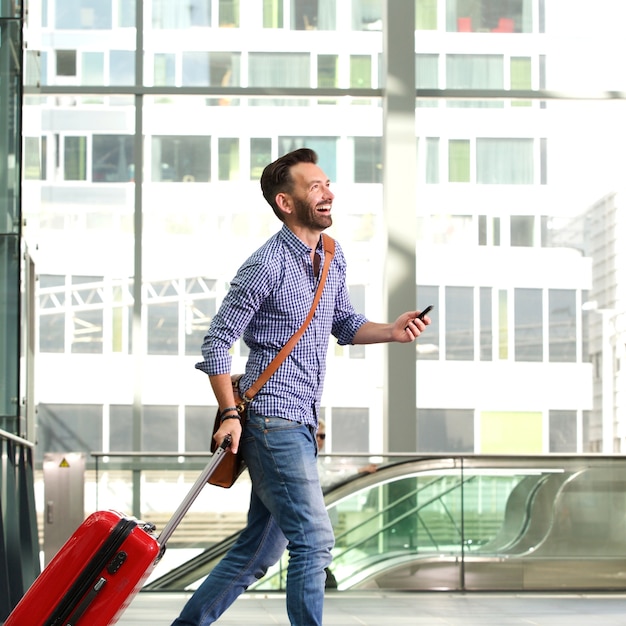 Photo smiling mature male traveler walking with suitcase and cellphone