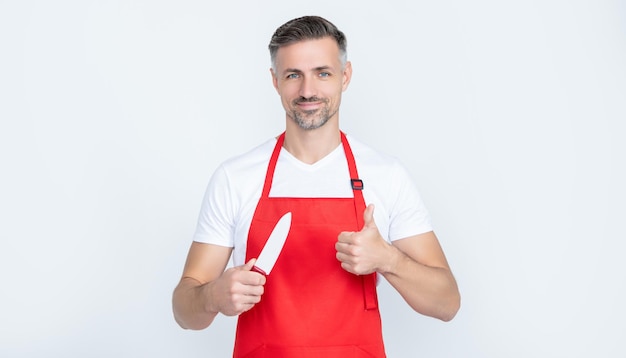 Smiling mature man cook in apron with knife on white background thumb up