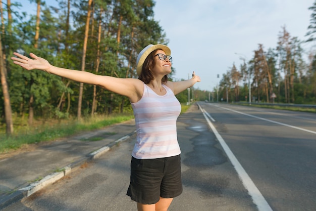 Smiling mature woman stands on the road, spread her arms out to the sides