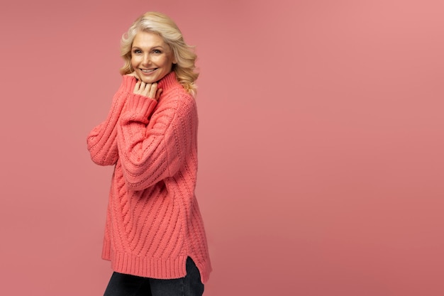 Photo smiling mature woman wearing warm winter sweater isolated on pink background