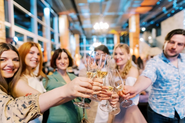 Smiling men and women clinking glasses of wine while standing in a restaurant