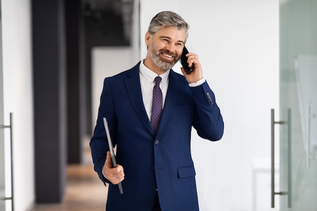 Smiling Middle Aged Businessman Talking On Cellphone While Walking Out Of Office