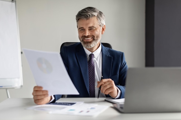 Smiling Middle Aged Businessman Working With Papers At Desk In Office