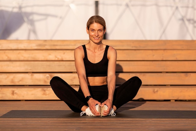 Smiling Middle Aged Female Athlete Stretching Leg Muscles While Training Outdoors