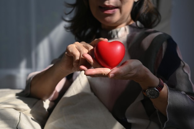 Smiling middle aged woman holding heart shape Elderly care insurance heart health and quality of life for elderly concept