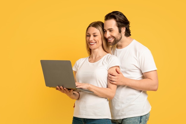 Smiling millennial caucasian man hugging woman in white tshirt and look at laptop making video call