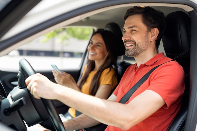 Smiling millennial couple sitting inside luxury car woman holding smartphone