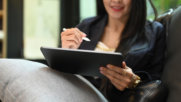 Smiling millennial woman using digital tablet while resting on couch at her personal office Cropped shot