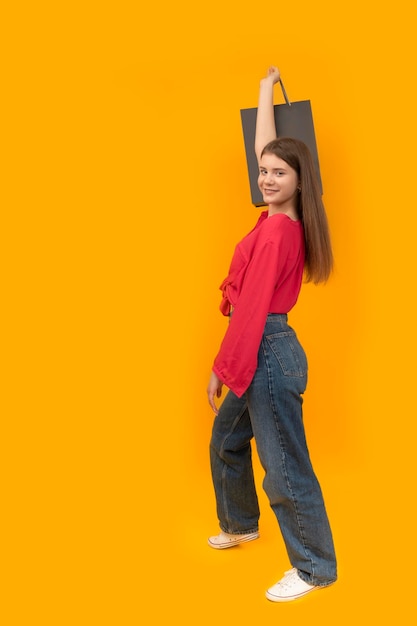 Smiling model in youth clothing holds paper black bags Yellow background Black Friday Shopping concept Vertical frame