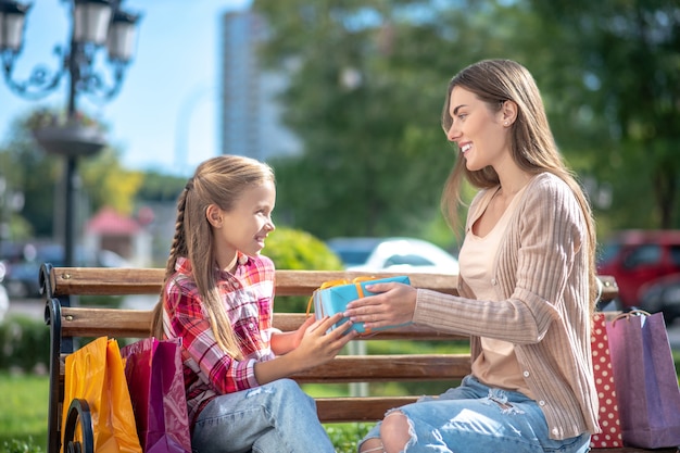 Smiling mom giving her daughter present on park bench