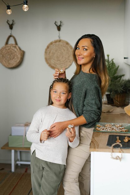 Smiling mom and her daughter are holding Christmas cookies in their kitchen