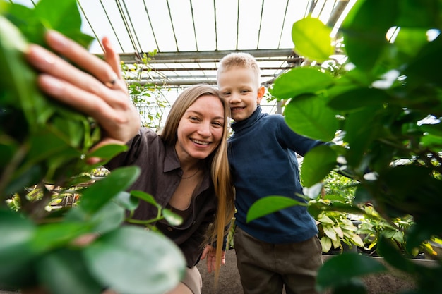 Smiling mom and son look out from behind the leaves of plants