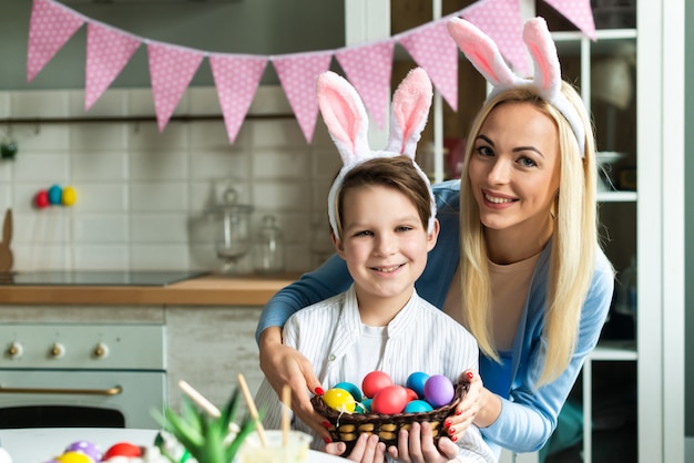 Smiling mom with son posing holding easter eggs in rabbit ears.