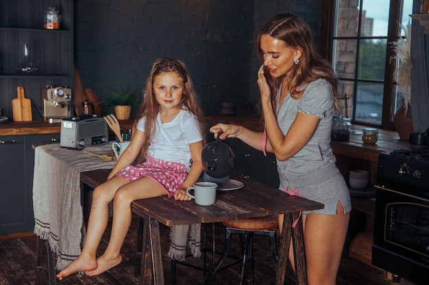 Smiling mother and daughter cooking and having fun in the dark kitchen interior