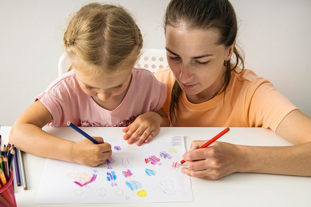 Smiling mother and daughter drawing together with colored pencils on paper Top view flat lay