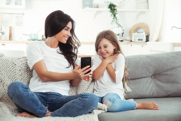 Smiling mother and little daughter playing games with smartphone