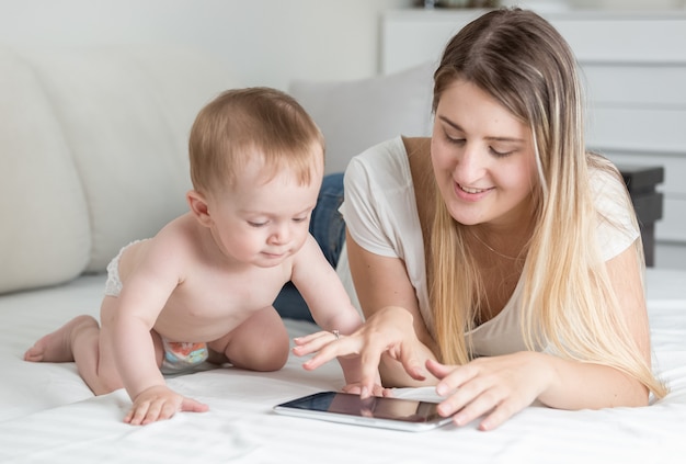 Smiling mother looking at her baby playing on tablet computer