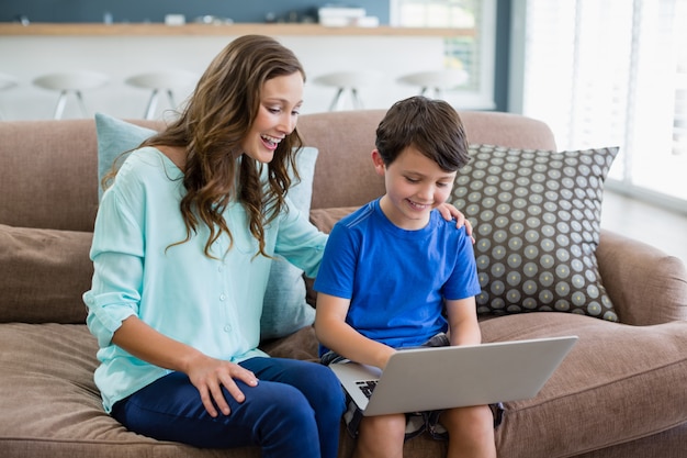 Smiling mother and son sitting on sofa using laptop in living room