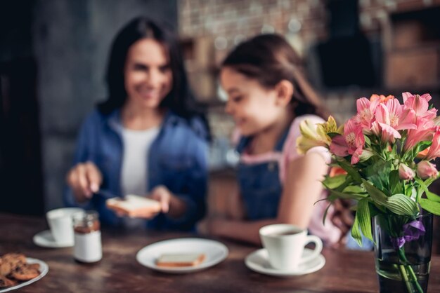 Smiling mother spreading toast with chocolate paste for her daughter in the kitchen