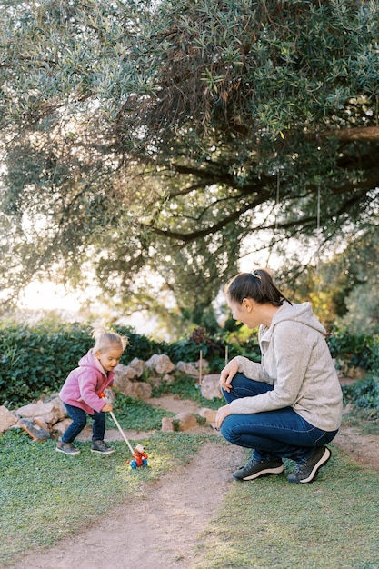 Smiling mother squatting near little girl pushing wheeled toy