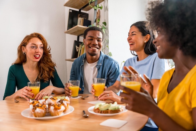 Smiling multiethnic friends over breakfast with orange juice and muffins at home