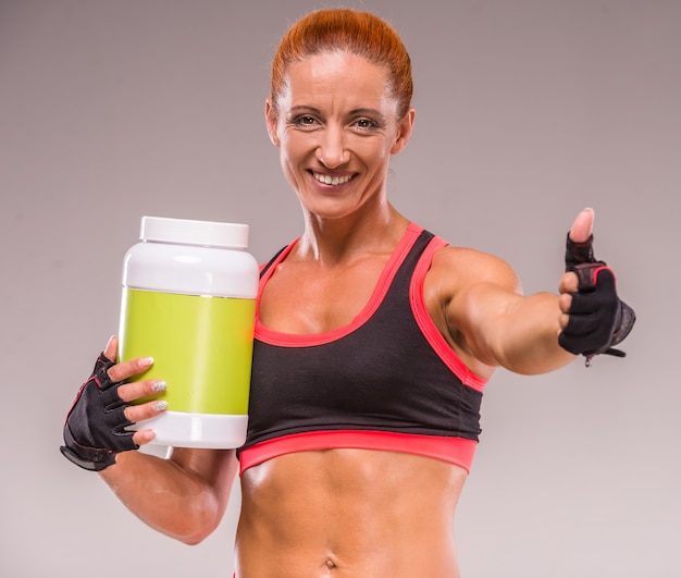 Photo smiling muscular woman with jar of protein.