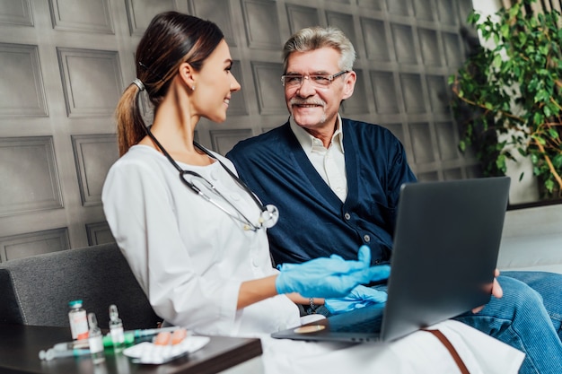 A smiling nurse communicates with an old patient and shows him his positive tests on the computer.