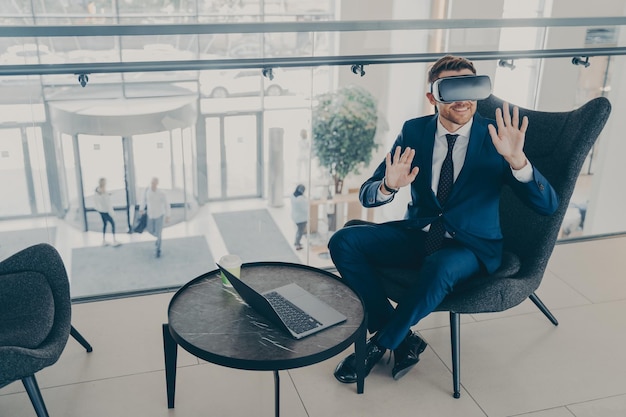 Smiling office worker sitting in company center lobby with laptop and VR headset goggles