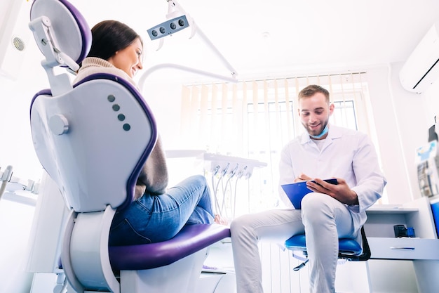 A smiling patient sits in a chair and answers a dentist's question. dentist at the workplace conducts a patient survey. History taking.