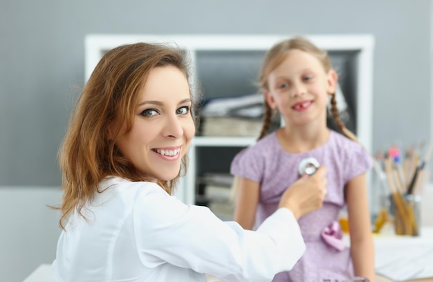 Smiling pediatrician doctor listen to girl breath and heartbeat with stethoscope