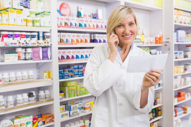 Smiling pharmacist on the phone reading prescription in the pharmacy