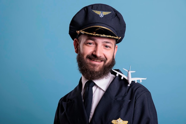 Photo smiling pilot in uniform with airplane model on shoulder portrait, aviation academy aviator playing with small plane. aircraft crew member with commercial jet toy, looking at camera