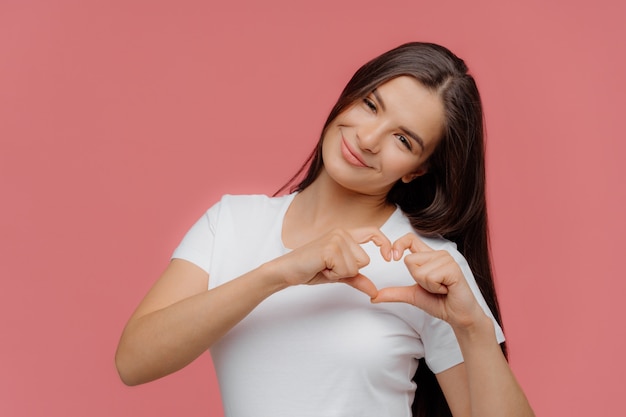 Smiling pleased brunette female model shapes heart sign