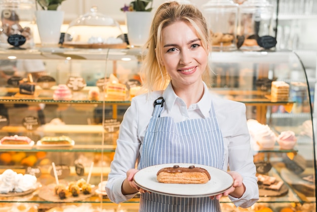 Smiling portrait of a female entrepreneur holding slice of cake on white plate