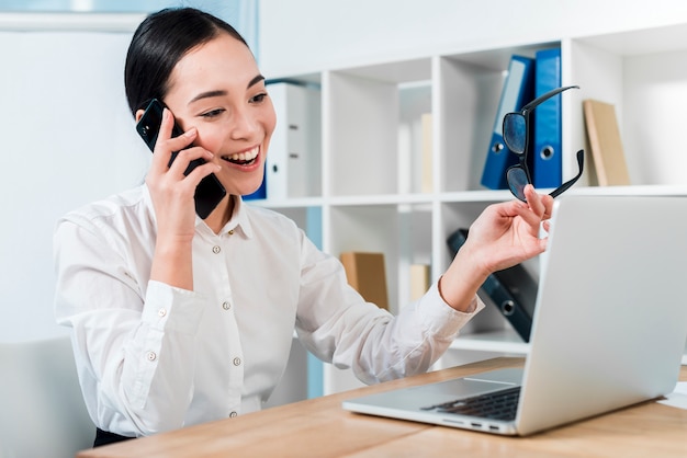 Smiling portrait of a young businesswoman talking on mobile phone looking at laptop