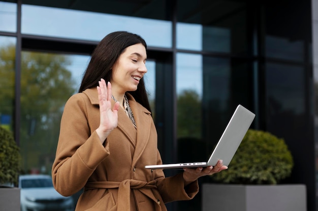 Smiling positive girl talking on video call using laptop outdoors on street Modern businesswoman