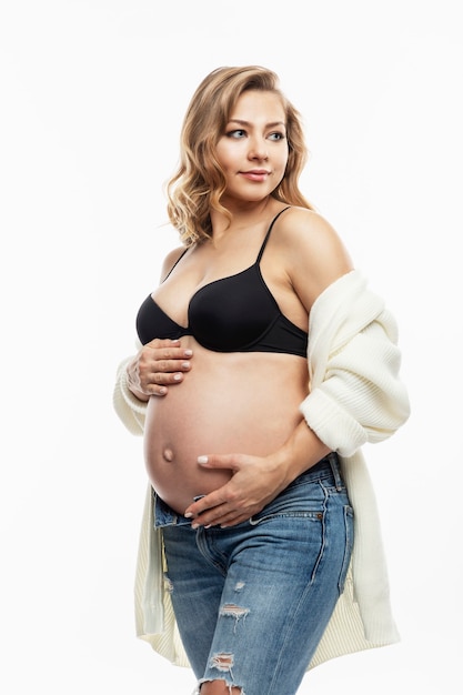 Smiling pregnant blonde woman in jeans on white