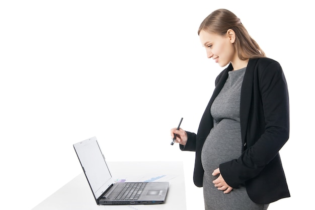 Smiling pregnant businesswoman with pen in hand looking at laptop