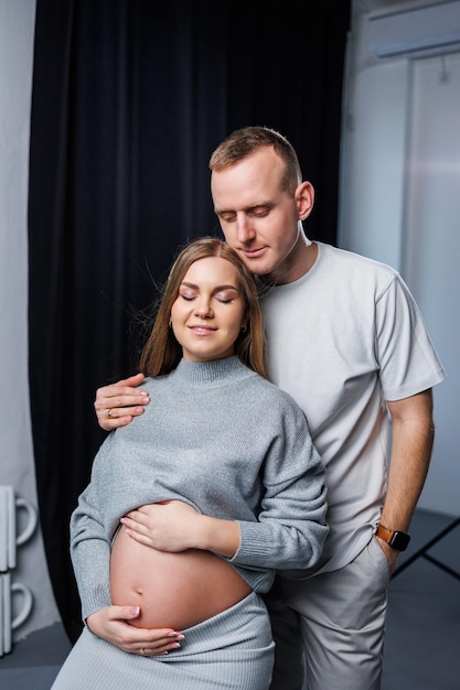 A smiling pregnant woman and her husband are standing in the studio and hugging Beautiful young attractive pregnant woman Family marriage childbirth concept Happy pregnant couple