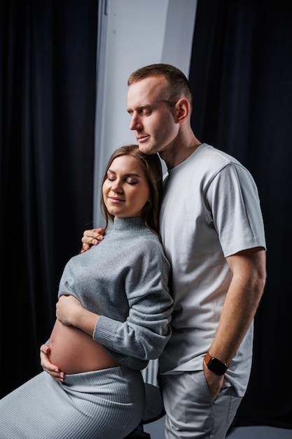 A smiling pregnant woman and her husband are standing in the studio and hugging Beautiful young attractive pregnant woman Family marriage childbirth concept Happy pregnant couple